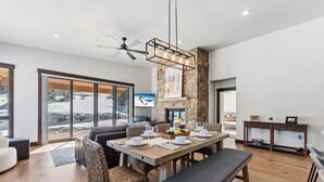 A modern dining area with a large table set for four, surrounded by wicker chairs, a bench, and a stone accent wall. - Summit County Gem |  Designer Kitchen + Great Views (Silverthorne)
