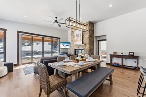 A modern dining area with a large table set for four, surrounded by wicker chairs, a bench, and a stone accent wall. - Summit County Gem |  Designer Kitchen + Great Views (Silverthorne)