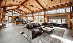 A spacious living area with a large leather sofa, a coffee table, and a dining table. There are large windows providing natural light and views of the outdoors. - Summit County Gem |  Designer Kitchen + Great Views (Silverthorne)