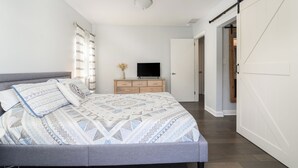 Un dormitorio con cama, televisor, cómoda y puerta corredera.