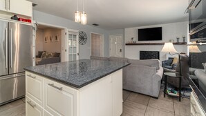 Una cocina moderna con una isla integrada, electrodomésticos de acero inoxidable y una zona de estar con sofá y sillones grises.