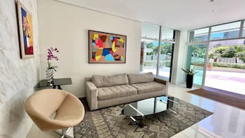 A modern living room with a sofa, a glass coffee table, a chair, a rug, and artwork on the walls.