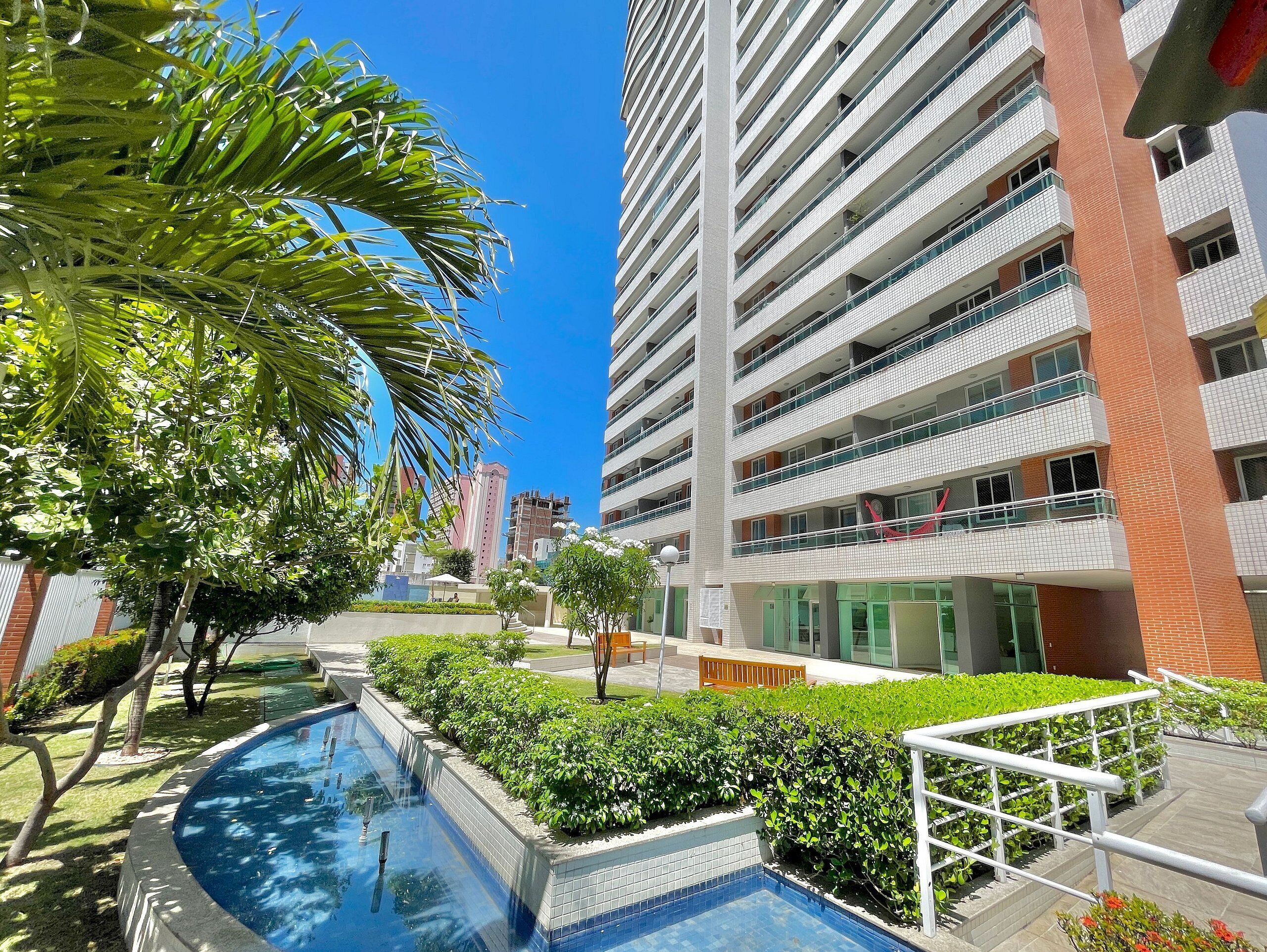 A modern building with multiple balconies, a swimming pool, and surrounding greenery.