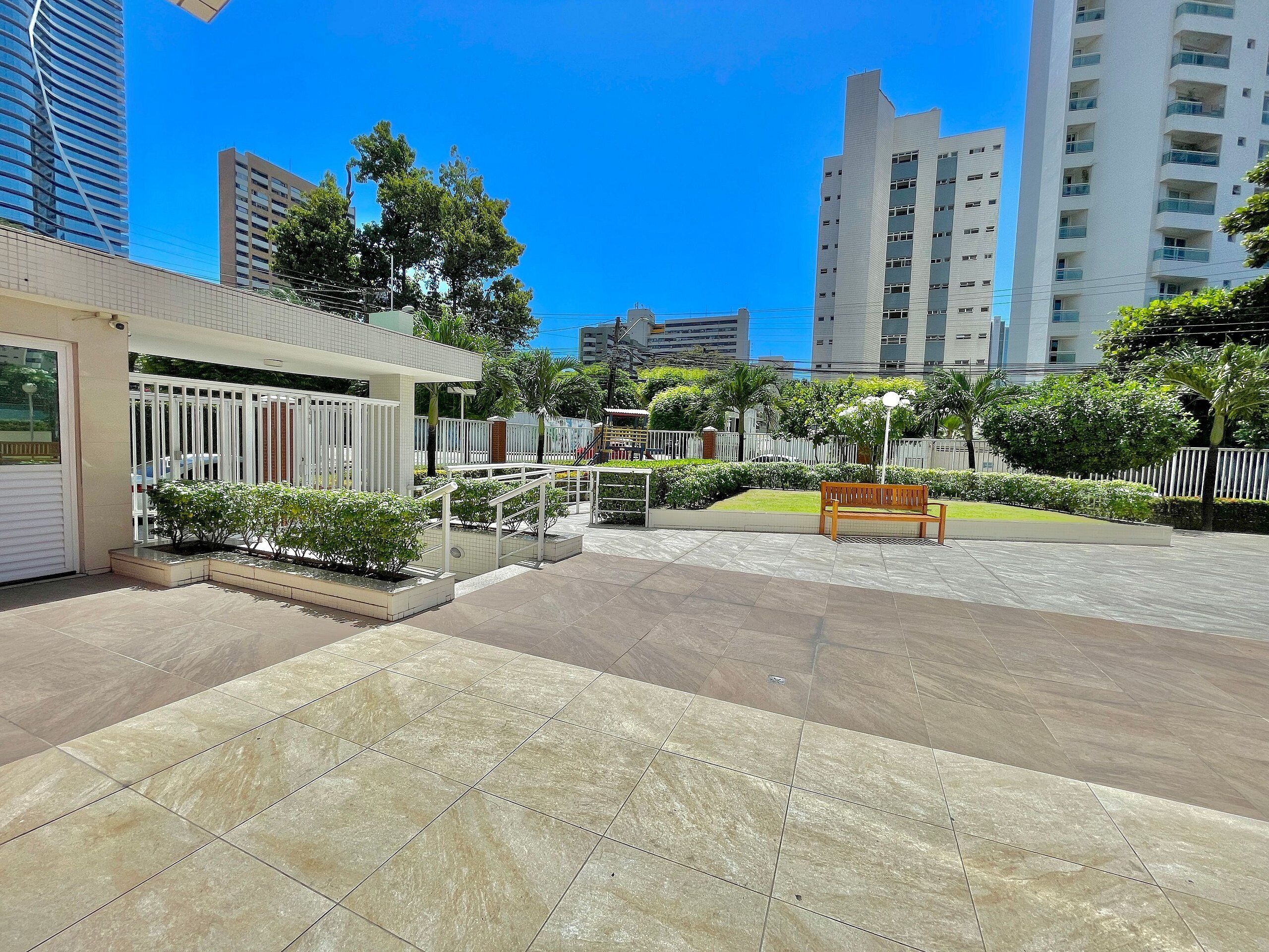 A courtyard with tiled flooring, a wooden bench, and a white fence.