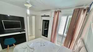 A hotel room with a bed, a TV mounted on the wall, a bathroom mirror, and a window with curtains. - Condominio Vivence (Fortaleza)
