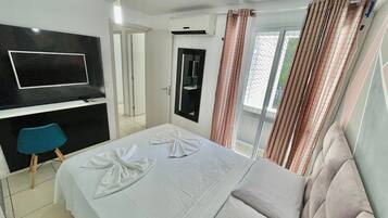 A hotel room with a bed, a TV mounted on the wall, a bathroom mirror, and a window with curtains.