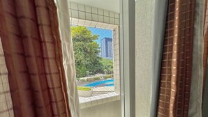 A view through a window with a metal grid, a pool, and a building in the background. - Condominio Vivence (Fortaleza)
