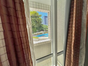 A view through a window with a metal grid, a pool, and a building in the background. - Condominio Vivence (Fortaleza)