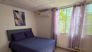 Une pièce comprenant un lit, un climatiseur fixé au mur, une fenêtre avec des rideaux et une porte dotée d’une poignée.