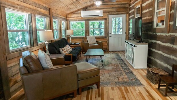 A log cabin interior with a sofa, armchairs, a coffee table, a TV, and a kitchenette. - Tranquil Mountainside Cabin in Charming Mountain View with AC (Mountain View)