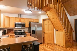 A kitchen with wooden cabinets, stainless steel appliances, a wooden staircase, and a wooden floor.