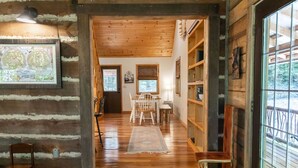 A log cabin interior with a wooden floor, a dining area with a table and chairs, and a bookshelf. - Tranquil Mountainside Cabin in Charming Mountain View with AC (Mountain View)