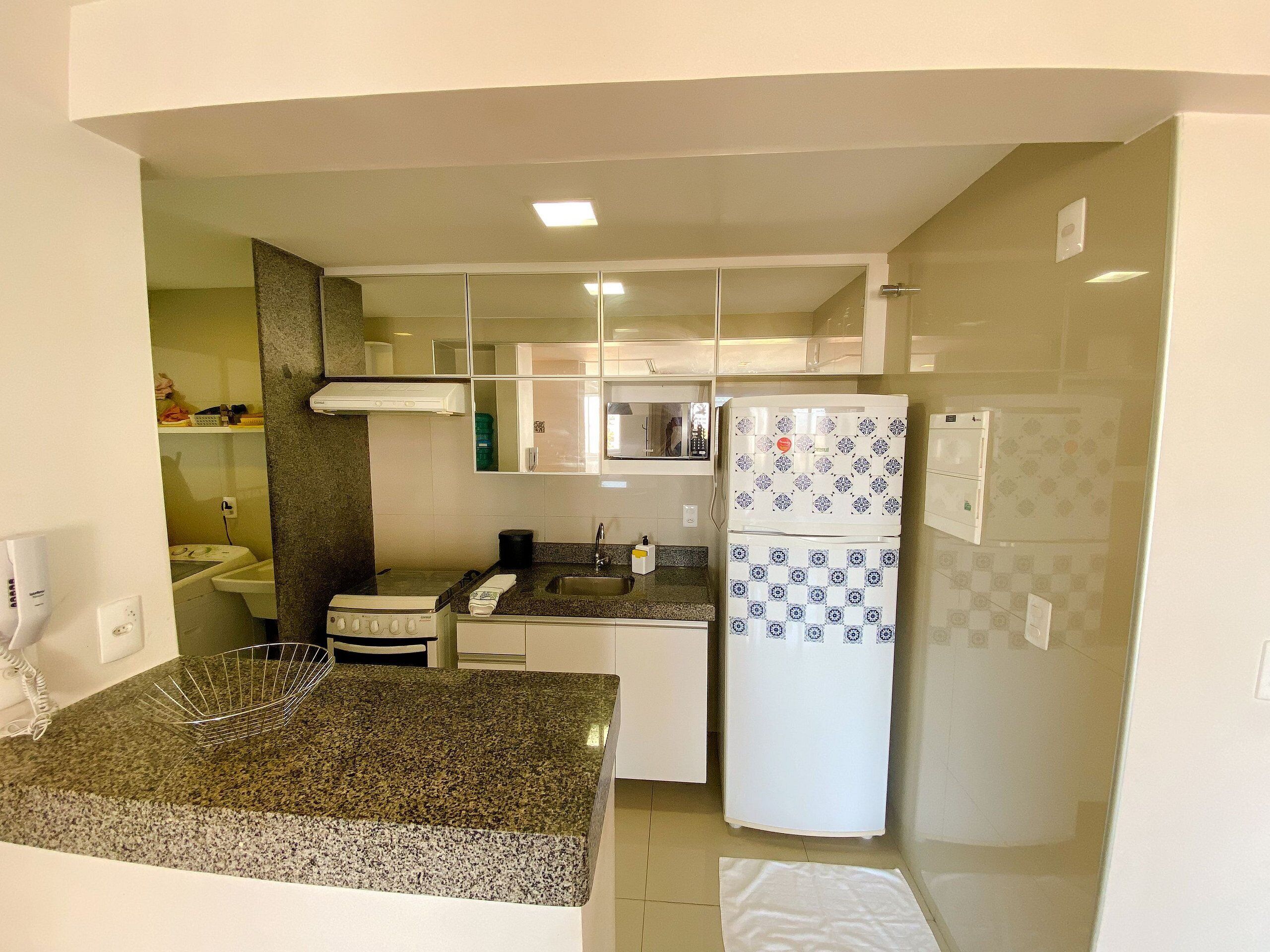 Una cocina compacta con encimera de granito, un refrigerador con puertas decoradas y un microondas.