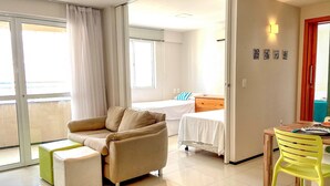Una camera d'albergo con un divano, un letto, un tavolo da pranzo con sedie e un balcone con tende.