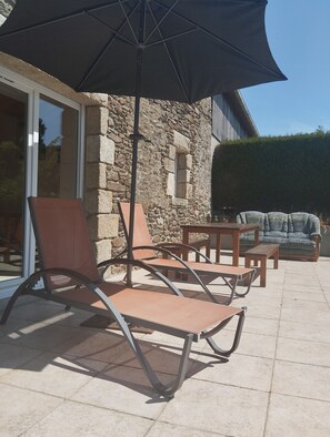 An outdoor patio with a stone wall, a glass door, and a seating area with a table and chairs. - Country House 10 Minutes from Saint-Jacut-de-la-Mer (Corseul)
