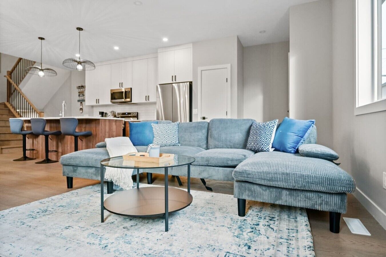 A modern living room with a sectional sofa, a glass coffee table, and a kitchen in the background.