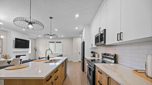 Een moderne keuken met een centraal eiland, roestvrijstalen apparatuur en hanglampen.
