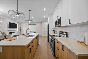 A modern kitchen with a central island, stainless steel appliances, and pendant lighting. - 16 Guests | 8BR | Game Rooms | King Beds (Calgary)