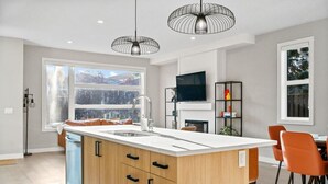 Een moderne keuken met een groot eiland, een eethoek met oranje stoelen en een aan de muur bevestigde televisie.