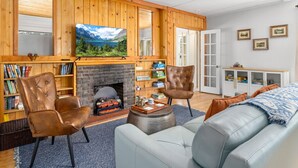 Una sala de estar acogedora con chimenea, sillones de cuero, un sofá y un televisor instalado en una pared de madera.