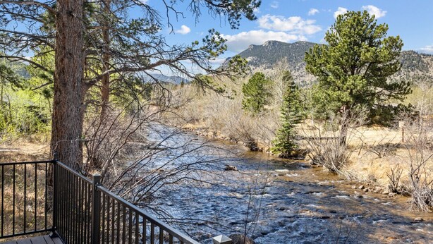 Un río con una pasarela de madera y barandilla, rodeado de árboles y montañas.