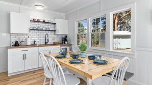 Una cocina moderna con armarios blancos, encimera de madera y una zona de comedor con una mesa dispuesta para dos personas.