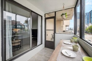 A modern kitchen with large windows, a dining table set with plates and cups, and a hanging plant. - Min to Saddledome | 2 Bed | Central (Calgary)