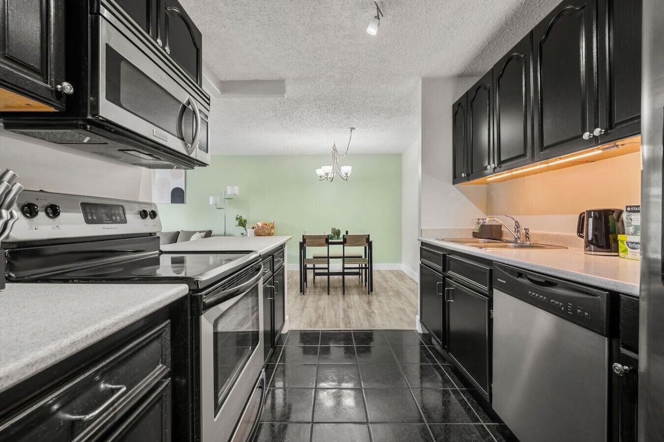 A modern kitchen with black cabinets, stainless steel appliances, and a dining area with a table and chairs.