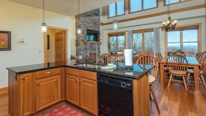 A spacious kitchen with wooden cabinets, a central island, a dishwasher, and a stone fireplace. - Mountain Retreat: Privacy & Comfort at 4,400 ft (Mars Hill)