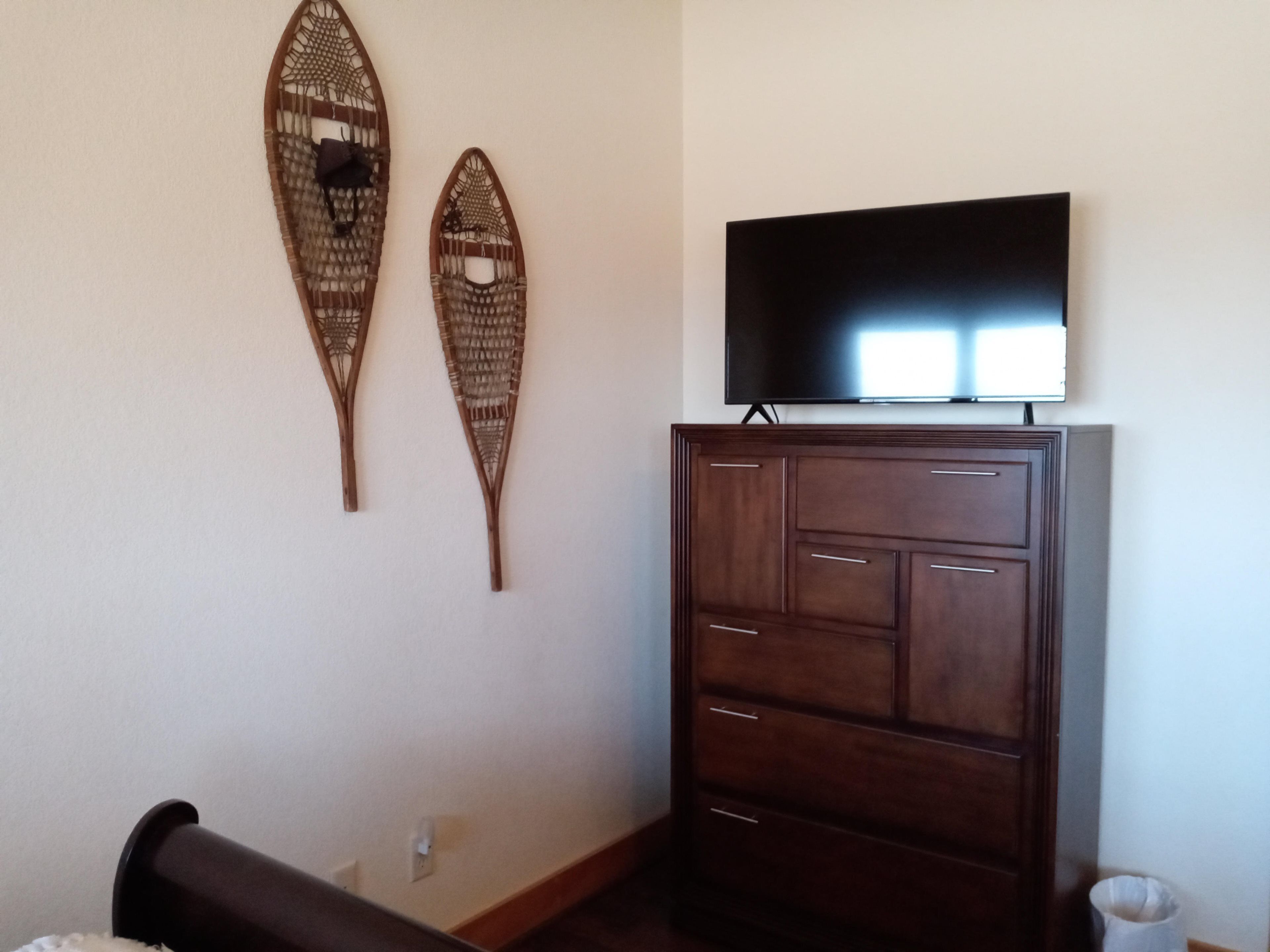 A room with a television on a cabinet, two wall-mounted decorative items, and a bed.