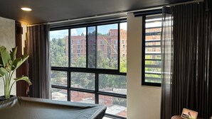 Habitació d'hotel moderna amb grans finestres, un llit, una taula petita i una planta en test.
