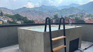 Terrat amb una font rectangular, una escala de fusta i vista a un paisatge urbà amb muntanyes de fons.