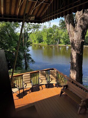 Eine Holzterrasse mit Bank und Stühlen, die auf einen stillen See mit umliegenden Bäumen blickt.