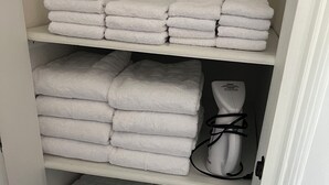 Een opslagruimte met netjes opgevouwen witte handdoeken op planken, een witte weegschaal en een witte waterdispenser.