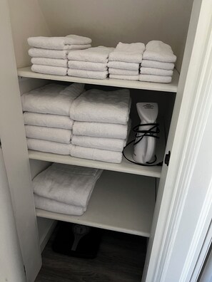 Un espace de rangement où des serviettes blanches, soigneusement pliées, sont disposées sur des étagères, ainsi qu’une balance blanche et un distributeur d’eau blanc.