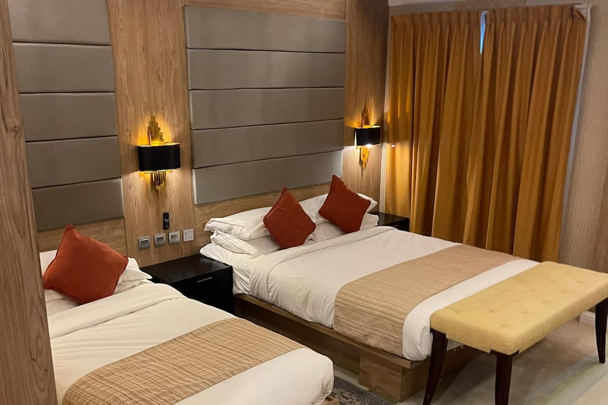Une chambre d’hôtel avec deux lits, un banc, un tapis et des lampes fixées au mur.