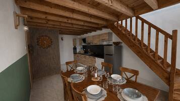 Un coin repas avec une table en bois dressée pour six personnes, une cuisine en arrière-plan et un escalier en bois.