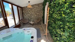 A spa room with a hot tub, stone walls, and a lush green vertical garden.