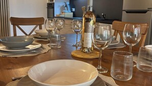 A dining table set with plates, cutlery, and wine glasses, with a bottle of wine and a kitchen in the background.