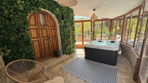 A spa area with a hot tub, wicker chairs, a patterned rug, and a wall covered in greenery.