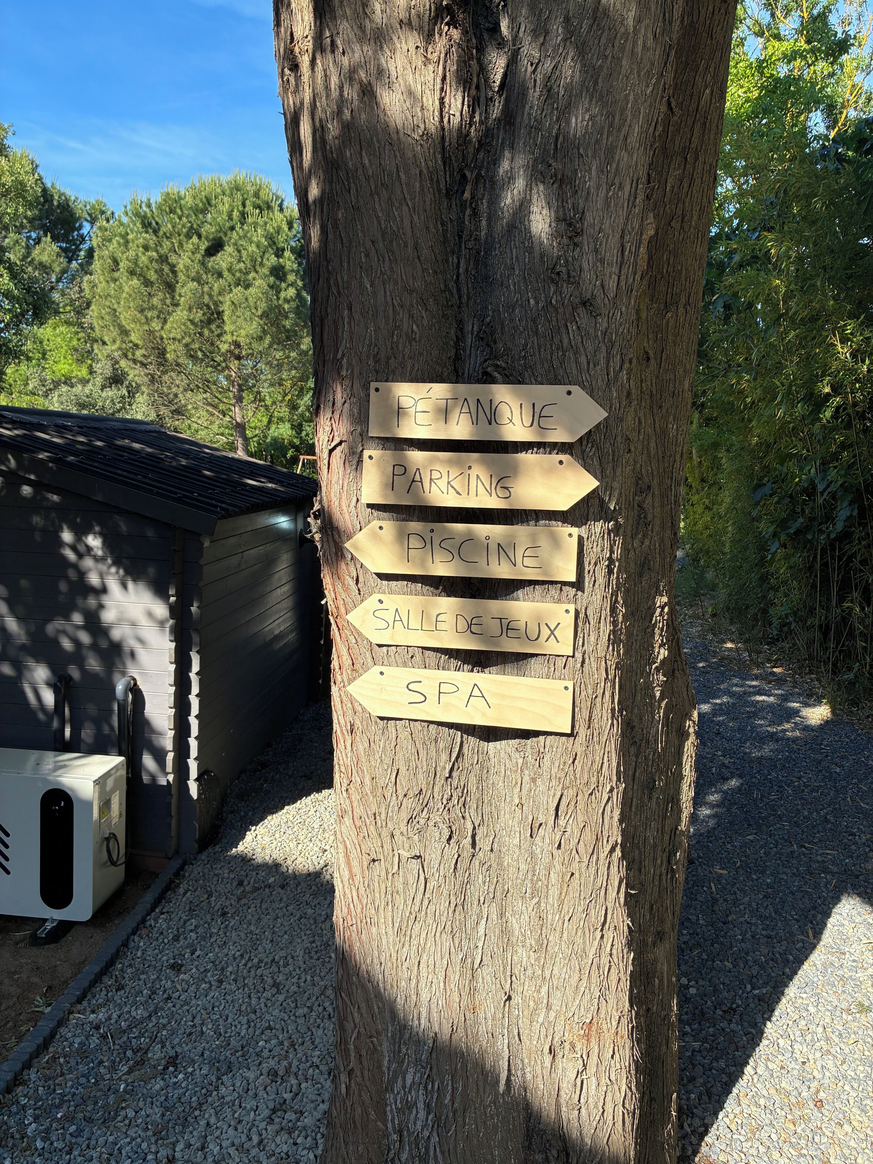 Un albero con cartelli direzionali che indicano servizi come un'area per la bocce, parcheggio, piscina, sala giochi e spa.