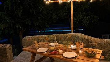 Un área de comedor al aire libre con un fondo de pared de piedra, mesa de madera y luces colgantes.