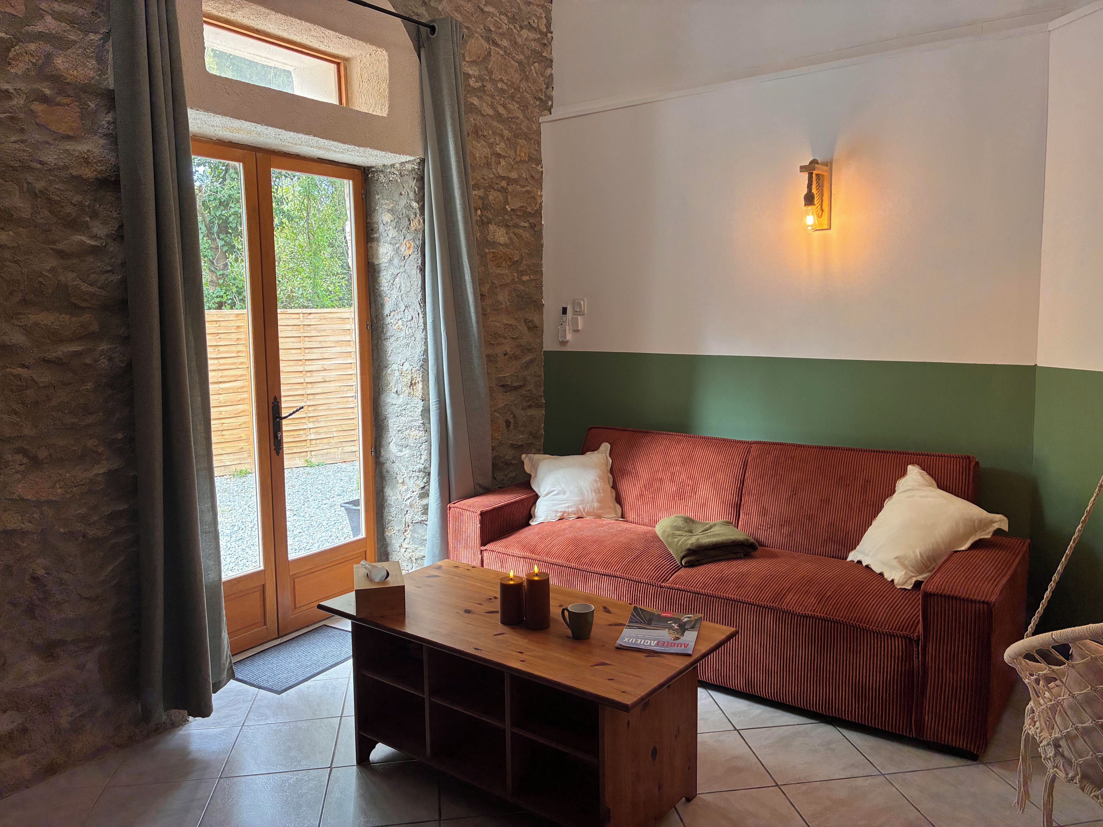 A room with a wooden coffee table, a red and white striped sofa, a green wall, and a window with curtains.