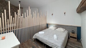 A bedroom with a bed, bedside tables, a wooden partition, and a stone wall.