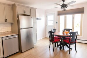 A kitchen with a stainless steel refrigerator, wooden cabinets, a dishwasher, and a dining area with a table and chairs. - 3 Bedroom Unit-Central Location (Moncton)