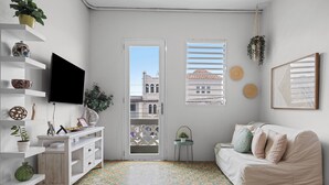A room with a white sofa, a TV, shelves with decorative items, a small table with a plant, and a patterned floor.