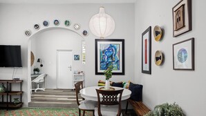 A dining area with a round table, chairs, a white ceiling light, and a wall decorated with framed artwork.