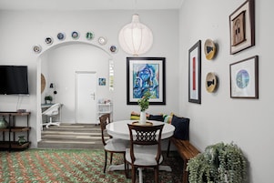 Un comedor con una mesa redonda, sillas, una lámpara de techo blanca y un muro decorado con obras de arte enmarcadas.
