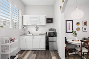 Una cocina compacta con armarios blancos, un refrigerador de acero inoxidable y un microondas.