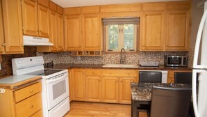 Una cocina con armarios de madera, estufa, microondas, lavaplatos y una zona de comedor con mesa y sillas.